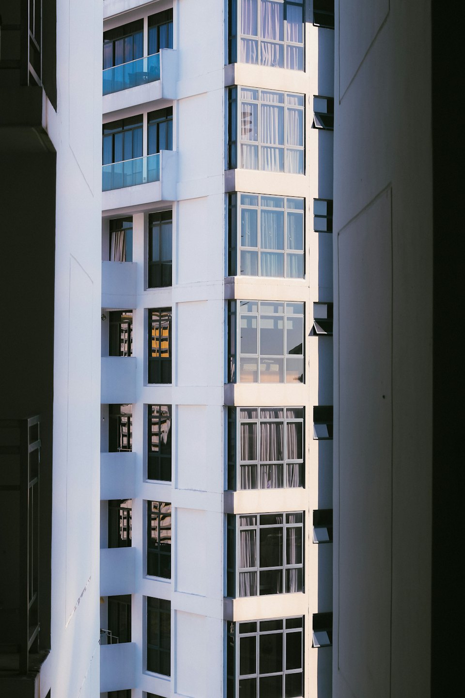 Edificio moderno de hormigón blanco con grandes ventanales y balcones azules.