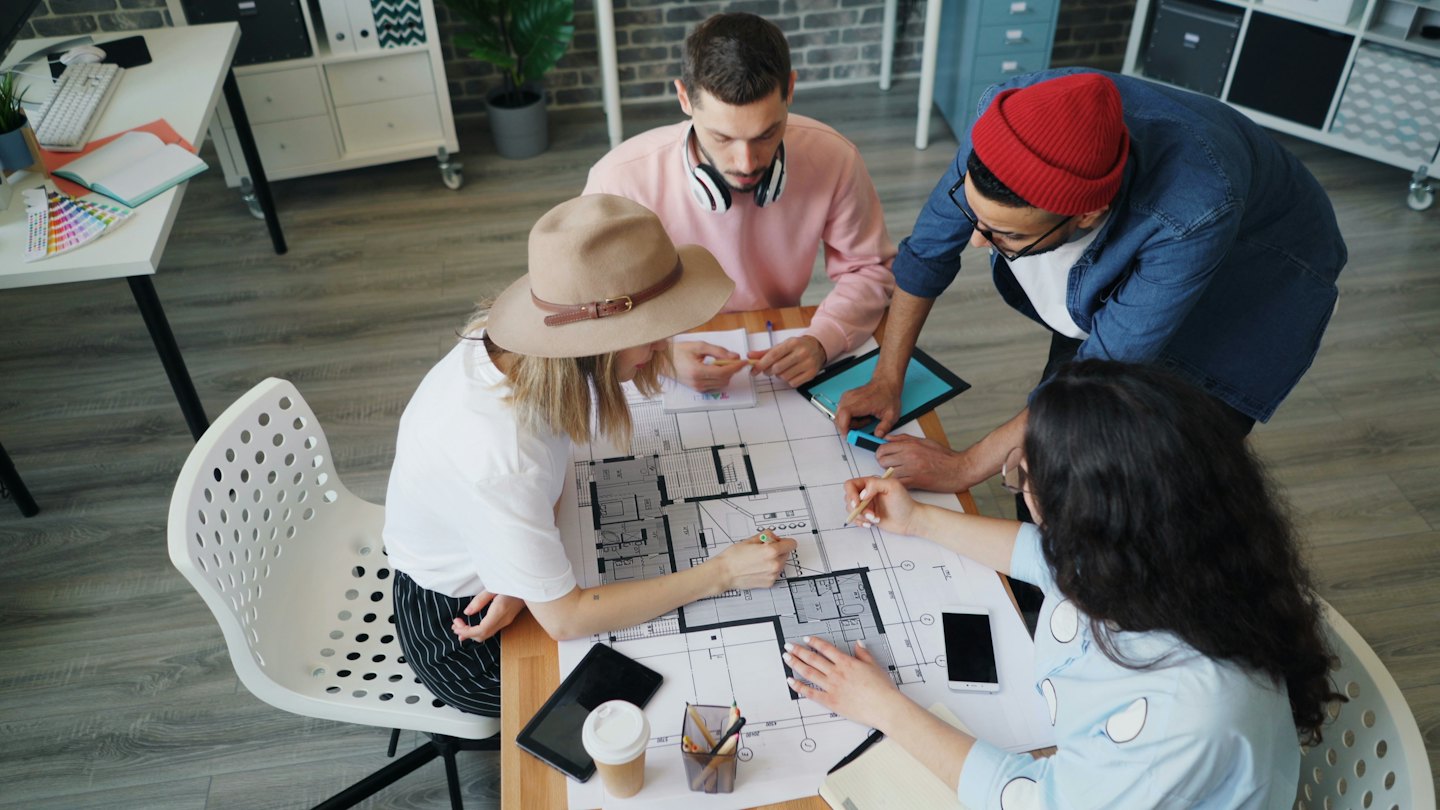 Cuatro adultos discutiendo planos sobre una mesa de madera.